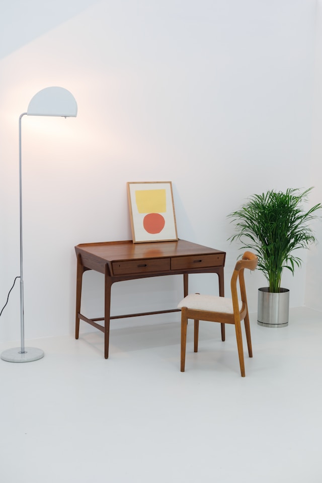 Table, chair, lamp, painting, and plant in a white room.